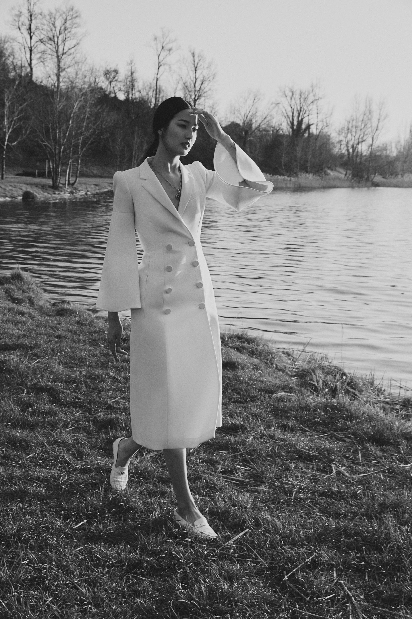 Ragazza con un elegante cappotto bianco cammina sul prato sulla riva di un fiume